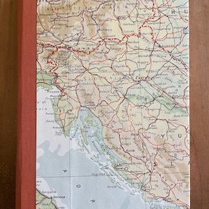 May include: A hardcover book featuring a vintage map of Austria, Slovenia, and Croatia on its front cover. The map displays geographical details, including cities, roads, and the Adriatic Sea. The book has a solid burnt orange fabric spine.