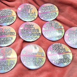 Könnte beinhalten: Eine Sammlung runder, pastellfarbener Buttons mit verschiedenen Sätzen in weißer Schrift. Sätze sind "Sensorische Verarbeitung Störung", "Nicht berühren" und "Unsichtbare Behinderung". Jeder Button hat die Worte "Bitte haben Sie Geduld".