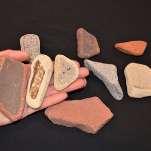 May include: A collection of ten small, irregularly shaped, flat stones in various shades of brown, red, and gray. The stones have a rough, textured surface.