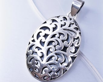 Può includere: Ciondolo ovale in argento con un intricato design traforato. Il ciondolo presenta un motivo dettagliato di linee e curve a spirale, creando un effetto pizzo. L'anello è un semplice anello lucido. Il ciondolo è esposto su uno sfondo bianco morbido.