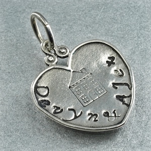 Peut inclure: Pendentif argenté en forme de cœur avec une maison gravée au centre. Le pendentif porte l'inscription "Dear Alea" sur le bord. Il est doté d'une boucle pour l'attacher à une chaîne.