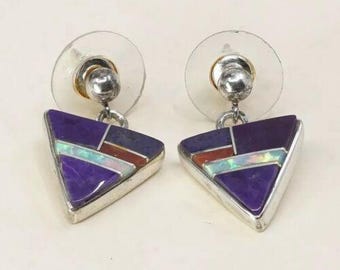 May include: A pair of silver-toned triangle earrings with a post back. Each earring features a geometric design with purple, dark blue, red, and iridescent white stone inlays. The earrings are set against a light background.