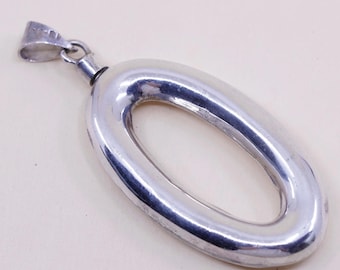 May include: A polished silver pendant in an elongated oval shape. The pendant has a loop at the top for a chain and a small, cylindrical detail at the base of the loop. The metal has a reflective surface.