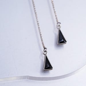 May include: A pair of silver-toned pull-through earrings featuring long, delicate box chains. Each chain terminates in a small, polished silver-toned triangular pendant with a smooth, solid black inlay centered within the metal frame.