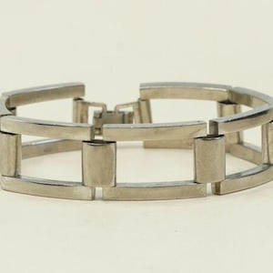 May include: A silver-toned bracelet with a rectangular link design. The bracelet features a series of connected rectangular links, creating a modern and geometric aesthetic. The clasp is visible, securing the bracelet. The overall design is sleek and minimalist.