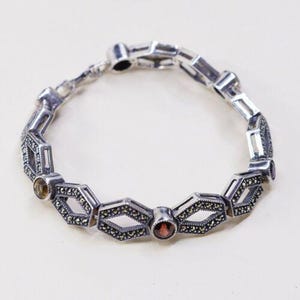 Puede incluir: Pulsera plateada con eslabones geométricos, detalles de marcasita y piedras preciosas. La pulsera presenta eslabones en forma de diamante, cada uno con una piedra preciosa central, diseñada para llevar en la muñeca.