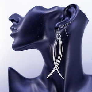 May include: A silver dangle earring featuring four slender, curved metal wires that converge at a single top ring. The earring hangs from a simple silver hook, creating a layered, fan-like shape that tapers toward the bottom in a sleek design.