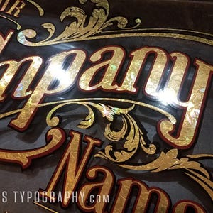 May include: A custom sign with the words "Your Company Name" in gold lettering with a red outline, set against a dark background. The design includes ornate gold flourishes and the website js typography.com.
