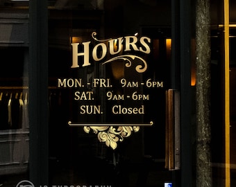 Pode incluir: Uma placa dourada com a palavra "HOURS" em uma fonte decorativa. A placa lista o horário comercial: de segunda a sexta-feira, das 9h às 18h; sábado, das 9h às 18h; domingo, fechado.