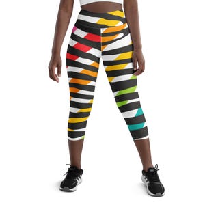 May include: Colorful capri leggings with a bold, abstract pattern. The leggings feature black, white, red, yellow, green, and teal stripes. The leggings are worn with a white crop top and black athletic shoes.