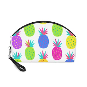 Può includere: Una pochette bianca con cerniera e cinturino da polso, caratterizzata da un motivo ripetuto di ananas stilizzati in colori vivaci tra cui verde lime, giallo brillante, magenta e blu, ciascuno sormontato da corone di foglie a contrasto color ottanio e rosa.