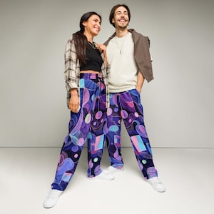 May include: Two people wearing matching abstract print pants with a dark blue background and purple, pink, and blue shapes. The pants have a drawstring waist and are paired with white sneakers. One person wears a black top and plaid shirt, the other a white shirt and brown jacket.