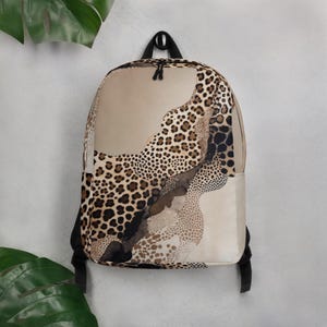 Könnte beinhalten: Ein beigefarbener Rucksack mit Leopardenmuster. Der Rucksack hat einen schwarzen Griff und Träger. Das Leopardenmuster weist braune und schwarze Flecken auf und ist ein stilvolles und funktionelles Accessoire.