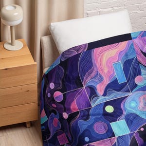 May include: A colourful abstract art blanket in shades of blue, purple, pink, and teal. The design features flowing lines, geometric shapes, and circular elements. The blanket is draped over a bed, showcasing its pattern.