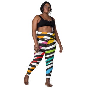May include: A woman wearing a black sports bra and colorful leggings. The leggings feature a bold zebra stripe pattern with vibrant colors including red, orange, yellow, green, and blue. The leggings have a high waist design.