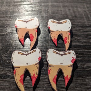 May include: Four cartoon teeth with red blood splatters on a brown wooden surface. The teeth are white with a yellow outline and are drawn in a cartoon style.