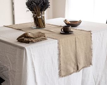 Puede incluir: Un mantel de lino blanco con un camino de mesa de lino marrón y una pila de servilletas de lino marrón. Una taza pequeña y un platillo marrones y un tazón están en el camino de mesa. Un jarrón con lavanda seca está en la mesa.