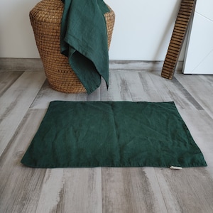 Può includere: Un runner in lino verde scuro posizionato su un pavimento in legno chiaro. Il runner è davanti a un cesto di vimini intrecciato con un panno di lino verde scuro drappeggiato sopra.