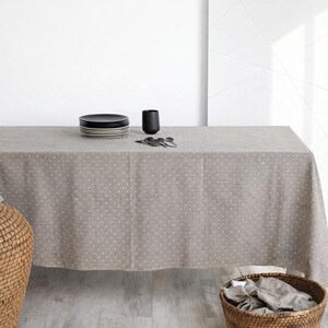 May include: A rectangular, taupe tablecloth with a white polka dot pattern covers a table. A stack of black plates, a black cup, and silverware are on the table. Wicker baskets are in the foreground.
