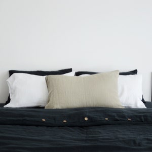 May include: A dark green linen duvet cover with button closures and a beige linen pillow on top of a white pillow. The bed is made with a black and white line art print on the wall behind it.