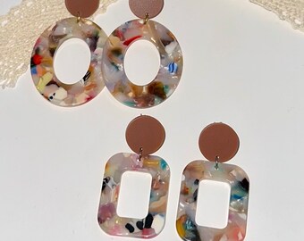 May include: A pair of brown and white resin earrings with a round and square shape. The earrings have a speckled pattern with a variety of colors, including pink, blue, and green.