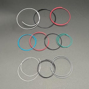 May include: Assortment of colourful and black wire spools, each wrapped in a circle. The spools are arranged in three rows, with the top row containing white, black, and red spools, the middle row containing blue, red, black, and green spools, and the bottom row containing white and black spools.