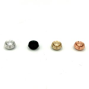May include: Four small, round, metal knobs in different colors: silver, black, gold, and copper. Each knob has a raised, circular top.