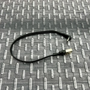 May include: A black USB charging cable with a right-angle connector on one end and a standard USB connector on the other. The cable is lying on a textured, gray surface.
