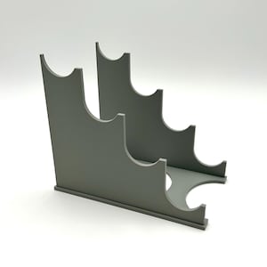 Puede incluir: Un botellero gris escalonado. Tiene cuatro aberturas curvas para sostener botellas. El diseño minimalista es de material sólido, adecuado para la decoración de cocinas o bares. Mide aproximadamente 30 cm de largo.