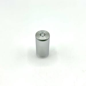 Puede incluir: Una batería cilíndrica plateada con una parte superior circular y un diseño texturizado.