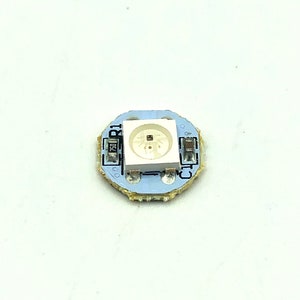 May include: A small, round circuit board with a white LED light in the center. The board is labeled "R1" and has several other components, including resistors and capacitors.