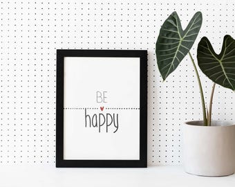 May include: A framed print with the words "BE happy" in a black frame. The text is in a playful font with a small red heart. A potted plant with large green leaves sits to the right.