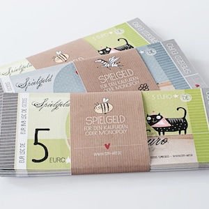 May include: A stack of colorful play money, featuring illustrations of a bee, a cat, and a zebra. The bills are labeled "Spielgeld" and "5 Euro", with text in German. The design includes a heart and the website www.sth-art.de.