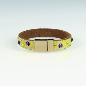May include: A gold leather bracelet with a magnetic clasp. The bracelet is decorated with purple and yellow rhinestones.