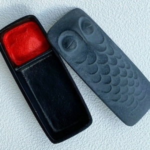 May include: Black ink and red inkwell set with an owl design on the lid. The lid is made of a textured material and features a raised owl design.