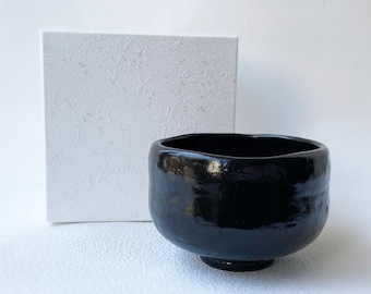 May include: A black ceramic tea bowl with a glossy finish. The bowl has a rounded shape and a slightly flared rim.