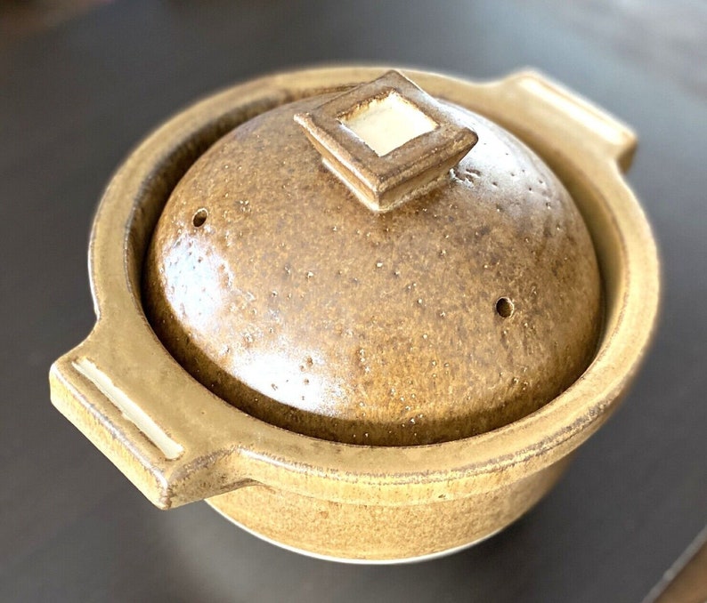 May include: A brown ceramic pot with a lid and two handles. The pot has a speckled glaze and a white interior. The lid has a square knob.