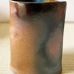 May include: A brown and blue ceramic vase with a rounded rectangular shape. The vase has a mottled glaze with shades of brown, blue, and green.