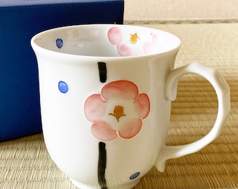 Puede incluir: Taza de cerámica blanca con un diseño de flores rosas y una línea negra. La taza tiene un patrón de puntos azules y un asa.