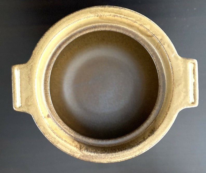 May include: A brown ceramic pot with two handles. The pot has a glazed finish and a slightly textured surface.