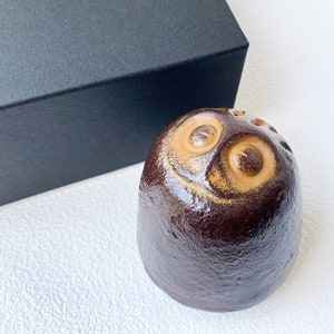 May include: A brown ceramic owl figurine with gold accents. The owl has large, round eyes and a slightly smiling expression.