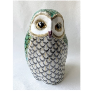 May include: A ceramic owl figurine with a white body, green and blue wings, and yellow and black markings. The owl has large, round, yellow eyes and a small, red beak.
