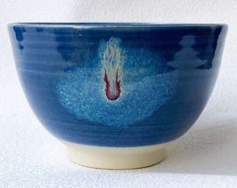 May include: A blue ceramic bowl with a white and red splatter design. The bowl has a white rim and base.