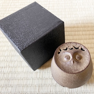 May include: A brown ceramic owl-shaped incense burner with a black box in the background.