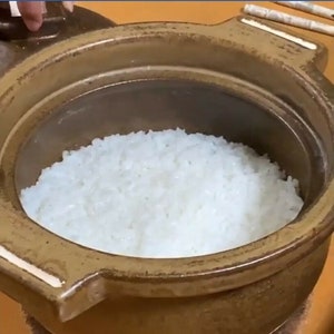 May include: A close-up of a brown ceramic pot filled with white cooked rice.