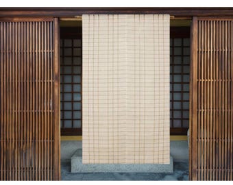 May include: A traditional Japanese doorway with wooden sliding doors and a beige checkered curtain hanging in the center. The wooden doors are a dark brown color and have vertical slats. The curtain is made of a woven material.