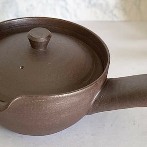 以下が含まれることがあります： 蓋と横の取っ手のある茶色の陶器製の急須。急須には側面に小さな注ぎ口があります。