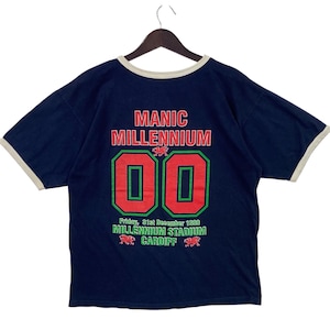 May include: Navy blue t-shirt with cream-colored trim and the text "MANIC MILLENNIUM" in red. Below are the numbers "00" in red with green borders. The text "Friday, 31st December 1999 MILLENNIUM STADIUM CARDIFF" is printed below.