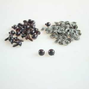 May include: A pile of brown plastic safety eyes with black pupils and a pile of silver plastic washers. Two individual brown plastic safety eyes with black pupils are in the center of the image.