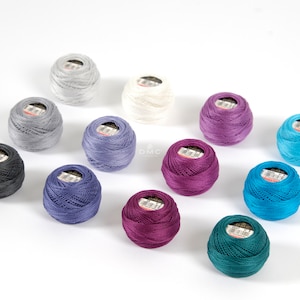 May include: Assortment of 12 spools of DMC embroidery floss in various colors, including teal, purple, blue, gray, and white.